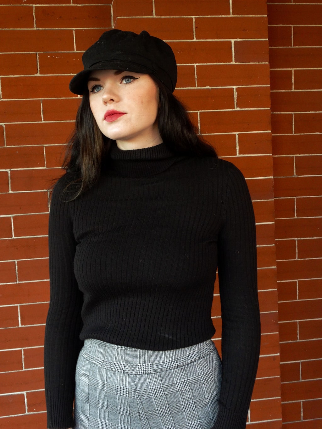 Mackenzie styles a tight black turtleneck sweater with high-waisted checkered pants and a black cabby hat.