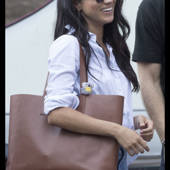 Meghan Markle at the Invictus Games in a blue button down shirt, a brown tote bag, and simple jeans with tortoiseshell sunglasses