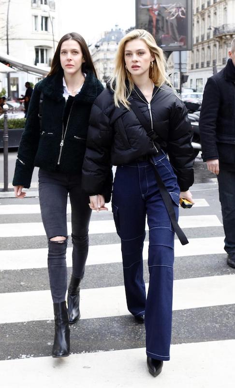 Nicola Peltz wearing a black cropped puffer jacket, white square neck cropped t-shirt, wide-leg cargo jeans, black platform ankle booties, and a black bum bag