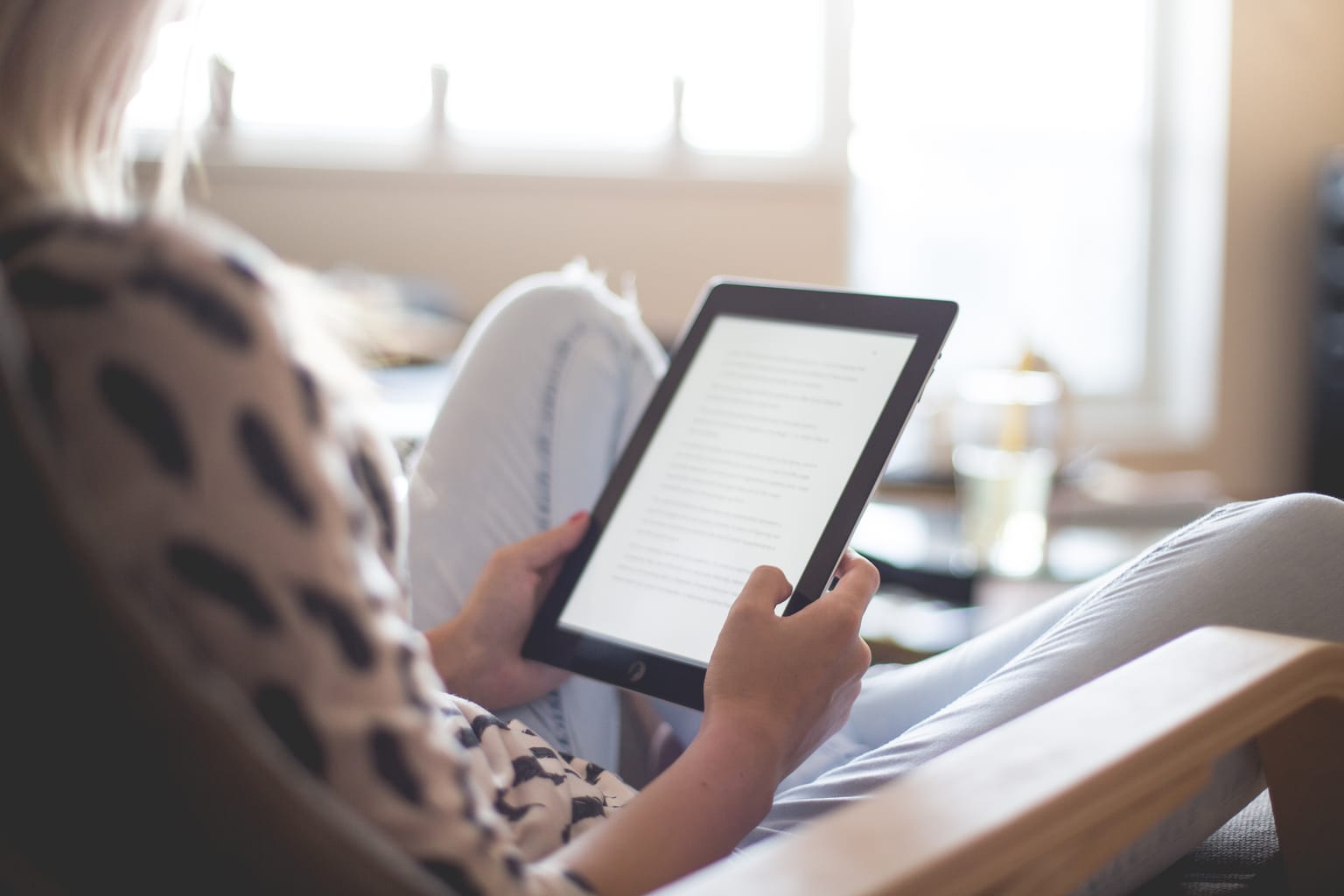 Woman sitting on a couch, reading a book on an iPad