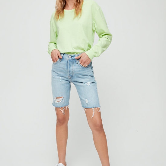 Woman wearing light neon green sweatshirt with light-wash denim Bermuda shorts and white sneakers