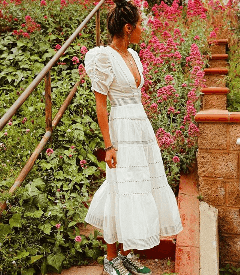 girl in longe white summer dress and green sneakers in front of a floral background