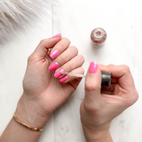 Girl painting glitter nail polish over bright pink nails