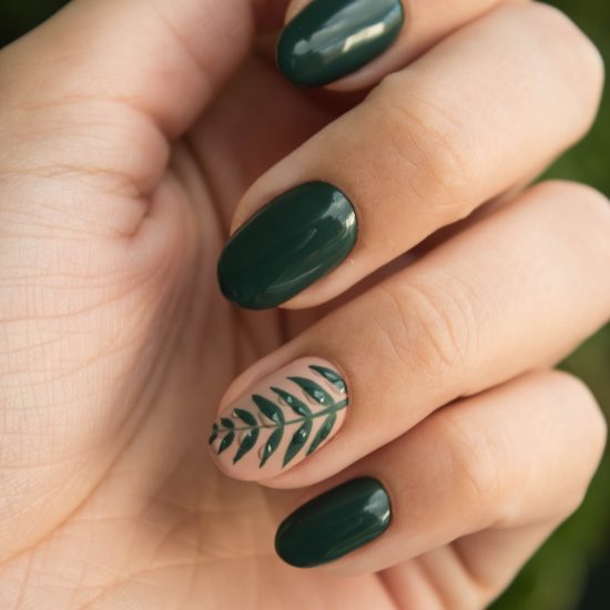 Close-up shot of dark green painted nails with leaf accent nail on ring finger