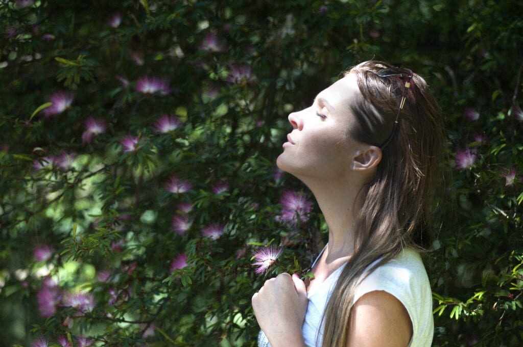 Woman facing sun with eyes closed surrounded by flowers